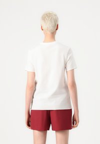 Witte katoenen T-shirt met korte mouwen, achteraan zichtbaar, aangevuld met maroon korte broek; eenvoudig ontwerp en zachte textuur.
