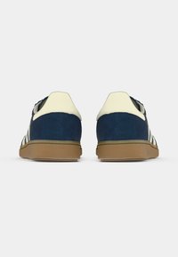 Blauwe suède sneakers met crèmekleurige accenten, voorzien van drie witte strepen, een afgeronde vorm en een getextureerde gumzool. Achteraanzicht weergegeven.