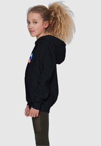 Svart hettegenser med et fargerikt sirkulært grafisk motiv på forsiden. Lange ermer og kengurulomme, brukt med grønne leggings.