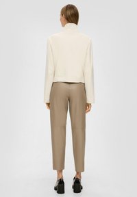 Lichtcreme kort jasje met hoge kraag, gecombineerd met strakke beige broeken. De outfit heeft gladde texturen en een op maat gemaakt ontwerp.
