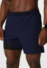 Marineblaue Sportshorts mit schwarzem Bund und integrierter schwarzer Innenbesatz. Verfügt über eine Seitentasche und einen gespaltenen Saum für mehr Beweglichkeit.