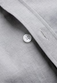 Gros plan d’un tissu gris avec un motif géométrique subtil, avec un bouton blanc à quatre trous cousu près d’une boutonnière.