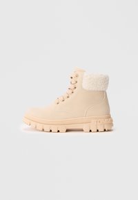 Bottine beige à lacets avec semelle épaisse, poignet en fourrure synthétique et logo embossé au talon, présentée en profil latéral.