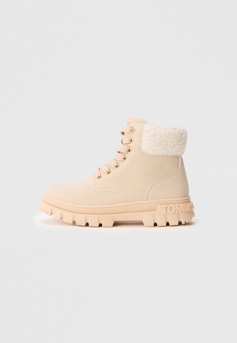 Bottine beige à lacets avec semelle épaisse, poignet en fourrure synthétique et logo embossé au talon, présentée en profil latéral.