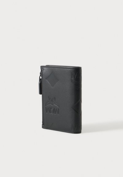 Portefeuille en cuir noir avec logo MCM embossé et motifs en diamant, debout sur un fond blanc uni.