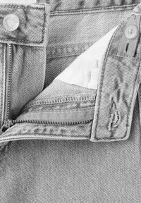 Svetlošedé rifľové nohavice so zipsom rozopnutým, viditeľným zipsom, gombíkom a vnútornou látkovou podšívkou.