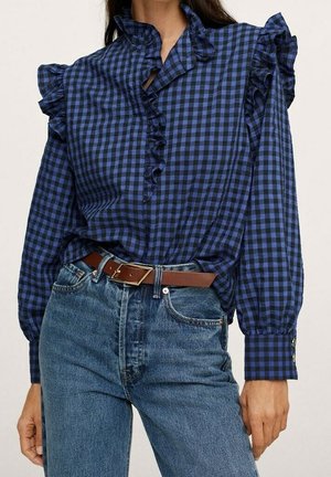 Blue and black checkered blouse featuring ruffled collar and sleeves, with a buttoned placket and comfortable fit, paired with blue jeans and a brown belt.