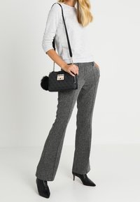 Sort skuldertaske med fluffy pom-pom detalje, guldfarvet hardware og logo; grå teksturerede buks med flæser; lys grå langærmet top; sorte hælede støvler.