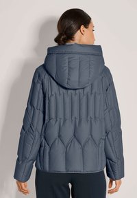Marineblauwe pufferjack met capuchon, gewatteerd ontwerp en elastische manchetten. Zachte textuur met diagonale stikpatronen op de rug.