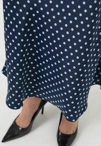 Granatowa sukienka w jasnobłękitne kropki, wykonana z gładkiej tkaniny, z rozkloszowanym dołem, zestawiona z czarnymi szpilkami.