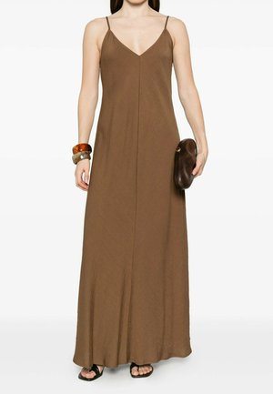 Donna che indossa un abito lungo marrone senza maniche con spalline sottili, sandali neri, grandi braccialetti e tiene in mano una borsa marrone scuro a clutch.