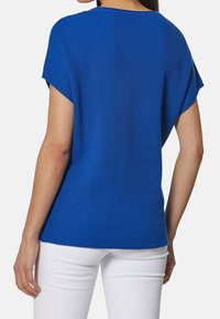 Krótki rękaw niebieski sweter z luźnym krojem, z okrągłym dekoltem i teksturowanym materiałem, w połączeniu z białymi spodniami.