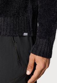 Czarny dziany sweter o teksturowanym, puszystym wykończeniu i ściągaczach na rękawach, zestawiony z ciemnymi spodniami z kieszenią na zamek i eleganckim krojem.