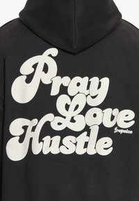 Schwarzer Kapuzenpullover mit großen weißen Buchstaben, die "Pray Love Hustle" in einem geschwungenen, stilisierten Schriftzug zeigen. Enthält das "Dropsize"-Logo in Weiß.