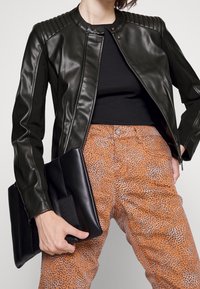 Chaqueta de cuero negra con hombros acanalados, combinada con pantalones marrones con estampado animal texturizado y un bolso de mano negro.