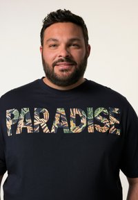 Tmavě modré bavlněné tričko s texturovanou grafikou "PARADISE" v zelených a oranžových listových vzorech, kulatý výstřih, krátké rukávy.