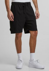 Svarta, strukturerade shorts med elastisk midja och dragsko. I kombination med vita sneakers och korta strumpor, vilket visar en avslappnad stil.