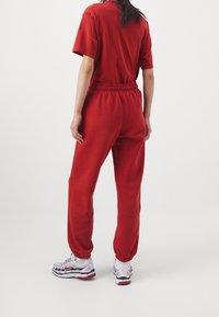 Rotes T-Shirt und passende Jogginghosen aus weichem Stoff, mit elastischem Bund und Bündchen. Kombiniert mit weißen und grauen Sportschuhen.