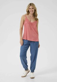 Svetlo roza top z čipkastim robom, v kombinaciji z ohlapnimi modrimi džins joggerji in belimi supergami. Obleka se ponaša z udobnim krojem in mehko teksturo.