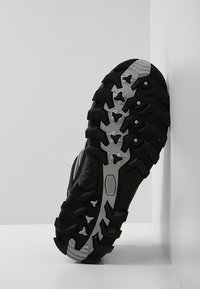 Schwarze Wanderschuhsohle mit tiefen Profilen für besseren Halt, grauen Akzenten und strukturierten Mustern. Mit einem markierten Logo an der Seite.