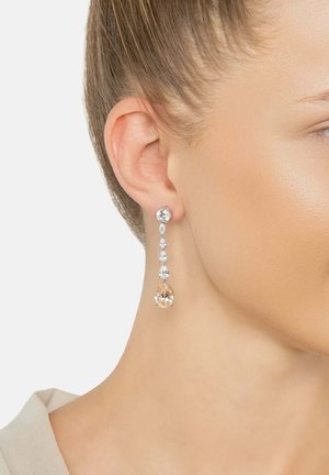 Das rechte Ohr einer Frau, geschmückt mit einem langen, hängenden Ohrring, der einen großen und fünf kleinere klare sowie blassrosa Edelsteine enthält.