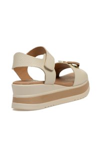 Sandalias de plataforma de cuero beige con tiras de velcro, un empeine texturizado y una suela de color marrón claro contrastante. Diseño elegante con detalles mínimos.