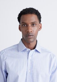 Blau-weiß gestreiftes Hemd mit Button-Down-Kragen. Glattes Material mit subtiler Glanz, verfügt über einen taillierten Schnitt und abgerundetem Saum.
