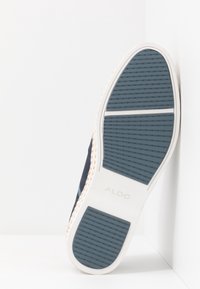 Sneaker in tela blu navy con suola in gomma bianca; presenta una superficie testurizzata e una striscia azzurro chiaro a contrasto lungo il lato.