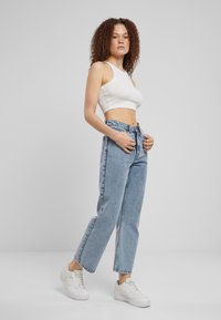 Top corto blanco ligero combinado con jeans rectos de cintura alta en un tono azul claro. La modelo lleva zapatillas blancas; fondo minimalista.