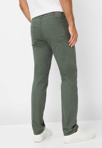 Groene katoenen broek met een slim fit, zichtbare stiksels, achterzakken en een logopatch op de tailleband. Draag met witte schoenen.
