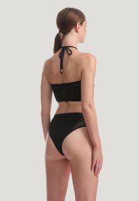 Svart bikiniset bestående av en bandeau-topp med halterneck och högmidjade botten. Tyget har texturerade accenter och utskärningsdetaljer.