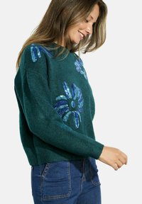 Maglione verde lavorato a maglia con applicazioni floreali in paillettes blu e viola. Polsini e orlo a costine, vestibilità comoda, con una texture morbida.