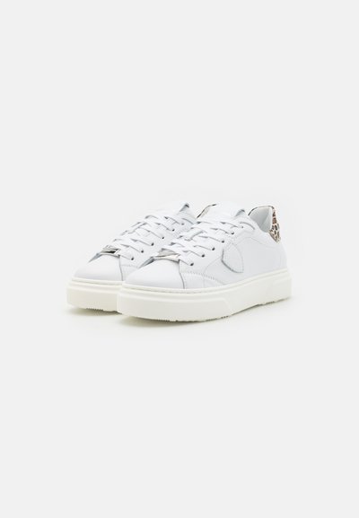 Sneakers bianchi in pelle con suola texturizzata, punta tonda e dettagli cuciti. Presentano un motivo decorativo sul tallone e lacci piatti.