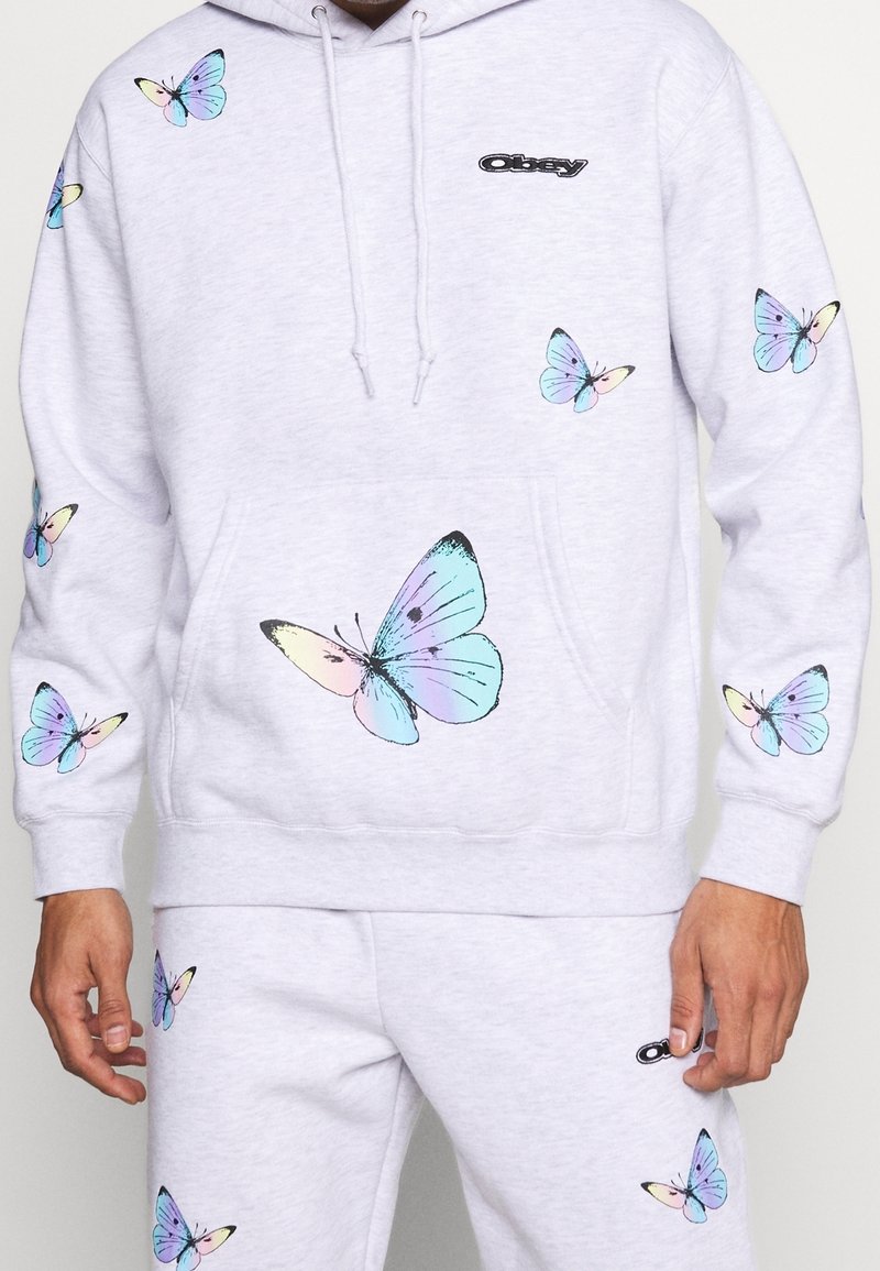 Hellgrauer Kapuzenpullover aus Baumwollmischung, mit mehrfarbigen Schmetterlingsmotiven und einem kleinen schwarzen Logo auf der Brust. Akzentuiert mit einer Kängurutasche.