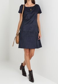 Námořnické modré šaty s krátkým rukávem z měkkého materiálu, s kulatým výstřihem a rozšířenou sukní. Doplněné hnědou křížovou taškou a kotníkovými botami.