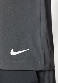 Nike siva športna majica iz teksturiranega materiala. Ima bel Nike logotip na spodnjem stranskem šivu in raven rob.