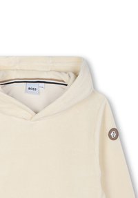 Felpa con cappuccio crema realizzata in morbido corduroy, con un logo ricamato sulla manica e un interno a righe bianche e nere.