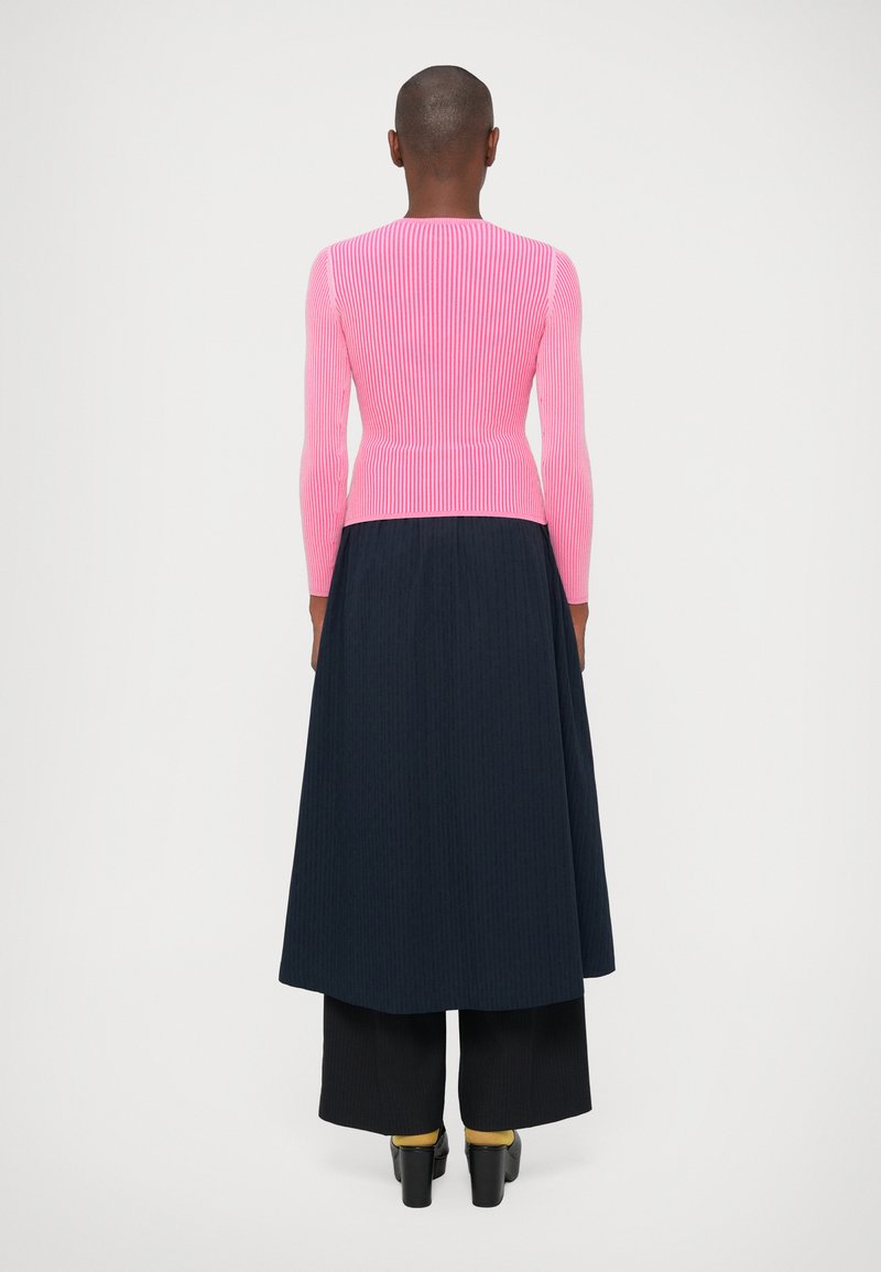 Long-sleeve top in ribbed bright pink knit, paired with a navy maxi skirt. Features a fitted bodice and flared lower section with subtle texture.