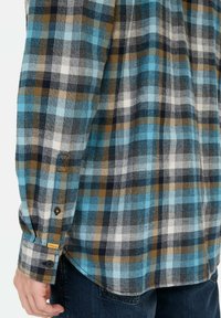 Flanellen overhemd in blauw, zwart, bruin en wit geruit patroon. Kenmerkt zich door knoopmanchetten met accenten en een gebogen zoom. Zacht, textuurstof.
