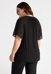Blusa nera plissettata con maniche corte e scollatura tonda, caratterizzata da un design fluido e un tessuto morbido e leggero.