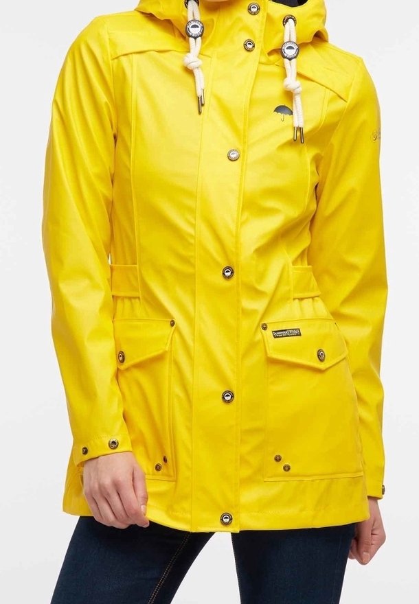 Veste imperméable jaune avec capuche, boutons-pression à l'avant, grandes poches à rabat, et cordons blancs sur la capuche, portée par-dessus un pantalon foncé.