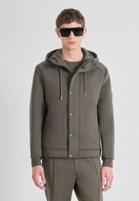 Olivgrüner Sweatjacke mit Kapuze, ausgestattet mit Druckknöpfen, Kordeln und Seiteneinsätzen; glatte Stofftextur.