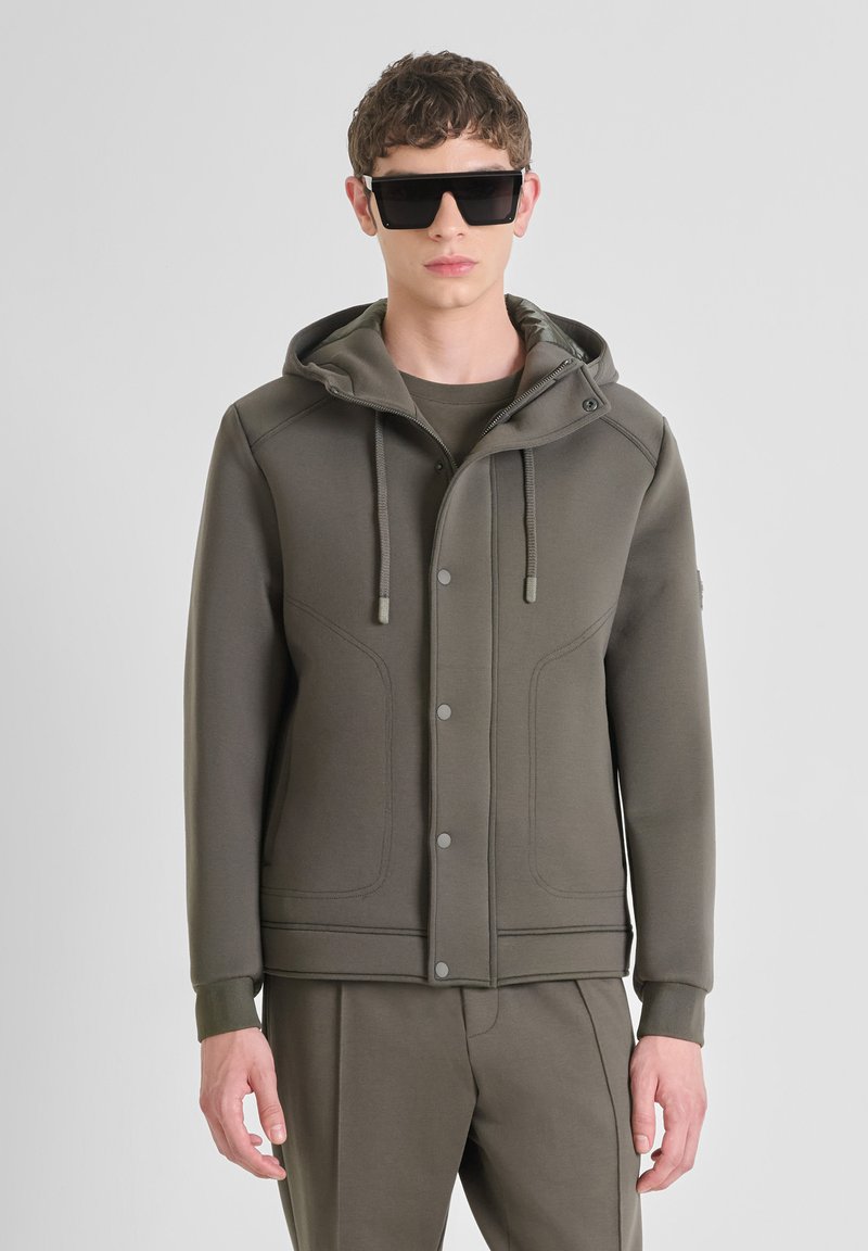 Olivgrüner Sweatjacke mit Kapuze, ausgestattet mit Druckknöpfen, Kordeln und Seiteneinsätzen; glatte Stofftextur.