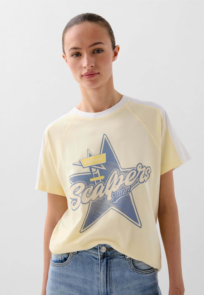 Geel T-shirt met korte mouwen, voorzien van een blauwe sterrenafbeelding met de tekst "Welkom" en "Scalpers", gecombineerd met lichtblauwe spijkerbroek.