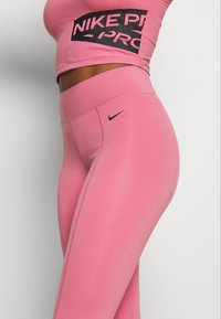 Top deportivo corto Nike Pro rosa con logo negro y leggings de cintura alta rosa a juego, ambos fabricados en tejido elástico para ropa de entrenamiento.