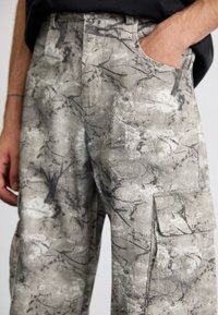 Pantalones cargo en una tela ligera y texturizada. Grises con un patrón abstracto en negro, con bolsillos laterales y un corte relajado.