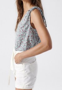 Top sin mangas de color azul claro con un patrón floral y escote en V, combinado con pantalones cortos de mezclilla blanca con dobladillo enrollado y bolsillos laterales.