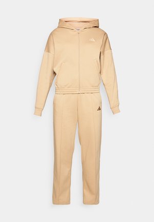 Ensemble de survêtement beige comprenant un sweat à capuche zippé avec une poche avant et un pantalon assorti. Fabriqué en matériau doux avec des poignets et une taille élastiques.