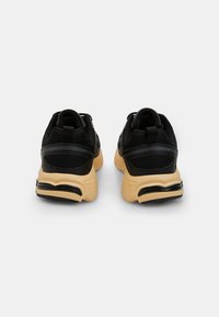Sneaker sportive nere con tomaia in rete e sintetico, dotate di un'intersuola beige ammortizzata e di una suola nera testurizzata.