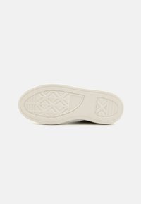 Suela de zapatilla de goma blanca con un patrón de agarre texturizado que presenta formas geométricas y el logotipo de la marca estampado cerca del talón.